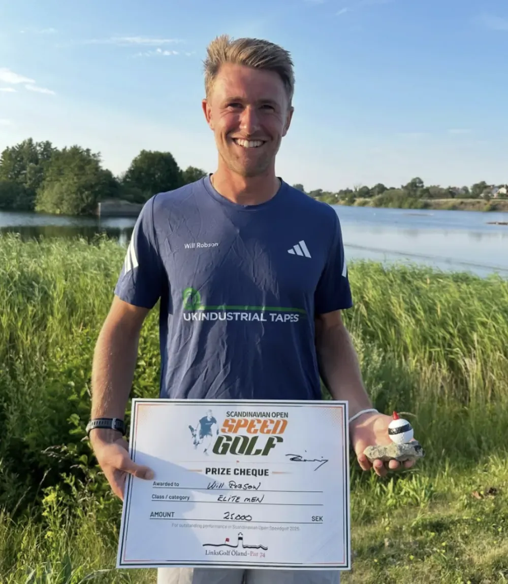 Will Robson holding his Scandinavian Open prize cheque beside the water.