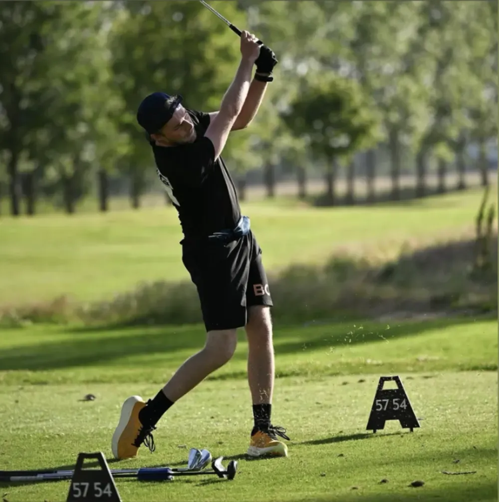 A speedgolfer follows through on a shot on a sunlit course.