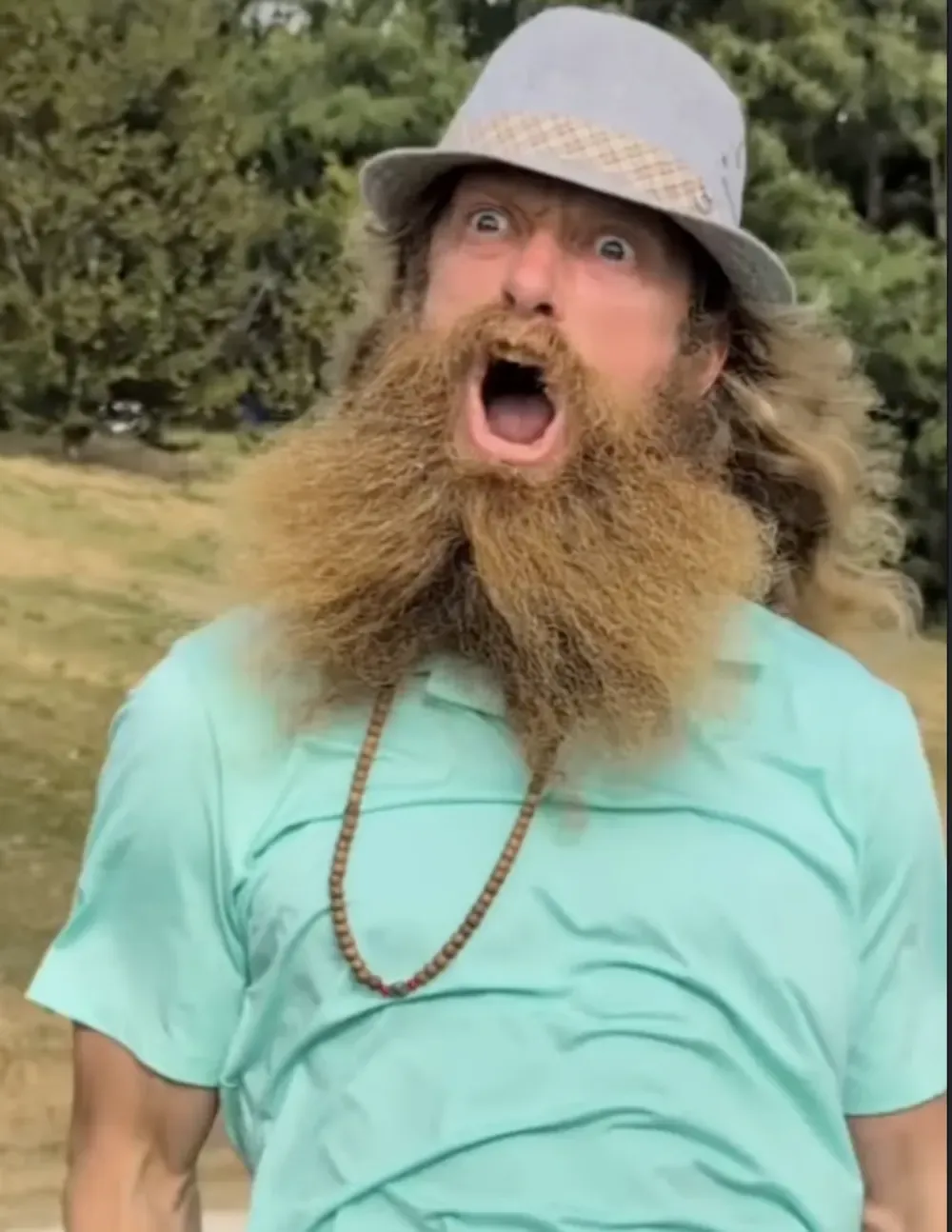 A bearded golfer in a brimmed hat reacts with wide-eyed surprise.
