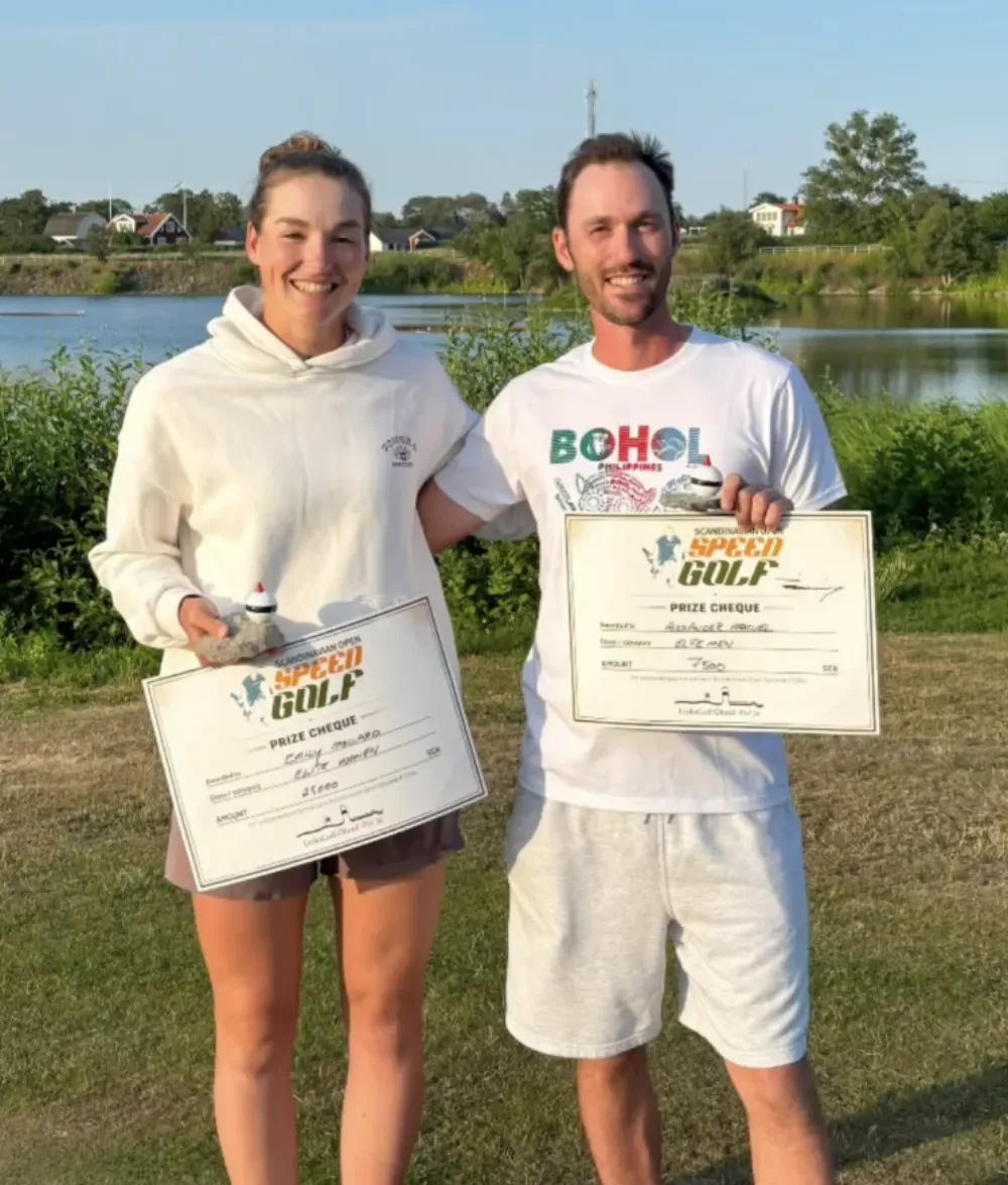 Two Scandinavian Open prize winners hold their cheques beside the water.