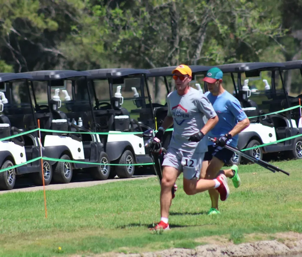 Two speedgolfers run past a row of golf carts during the U.S. Open pairs event.