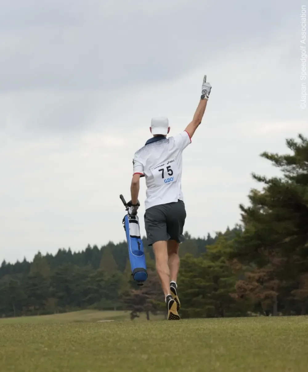 A speedgolfer walks away from a course carrying a blue golf bag.